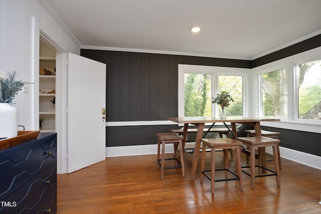 dining area featuring hardwood / wood-style floors, breakfast area, crown molding, and wood walls