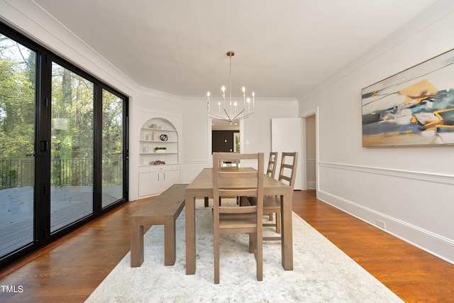 dining room with crown molding, hardwood / wood-style floors, a chandelier, and built in features