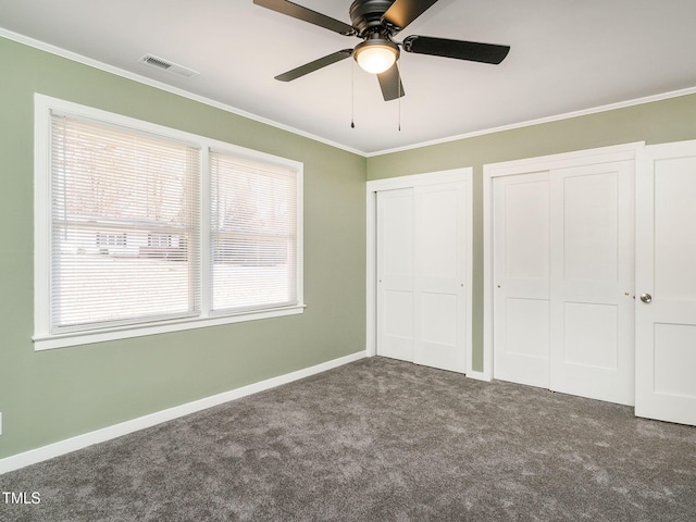 unfurnished bedroom featuring ceiling fan, crown molding, dark carpet, and two closets