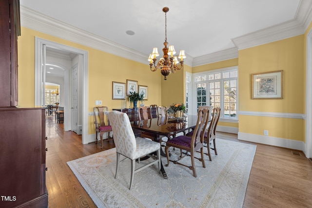 dining space with crown molding, a notable chandelier, and light hardwood / wood-style flooring