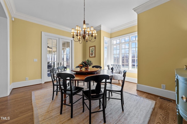 dining space featuring wood-type flooring, ornamental molding, french doors, and a notable chandelier