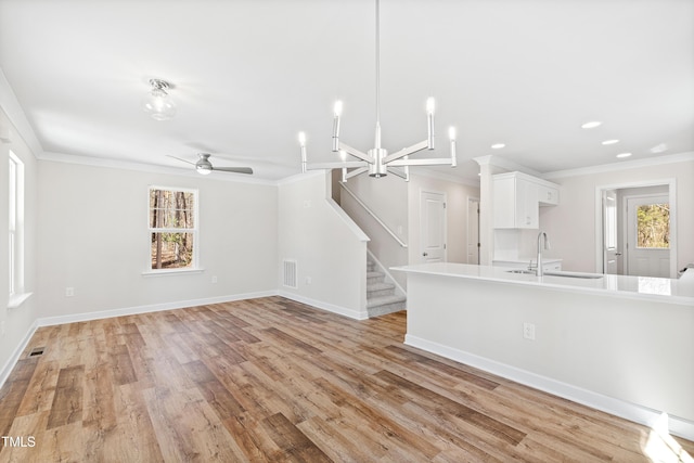 unfurnished living room with a sink, visible vents, light wood-style floors, ornamental molding, and stairway