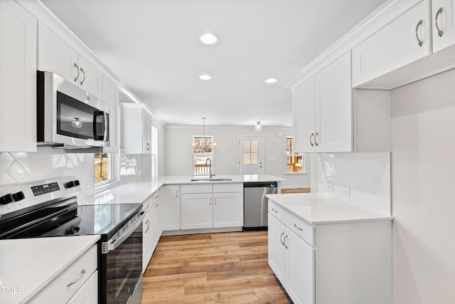 kitchen with appliances with stainless steel finishes, light wood-style floors, white cabinetry, a sink, and a peninsula