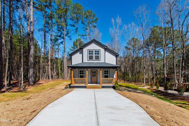 view of front of home with a porch, driveway, board and batten siding, and a wooded view