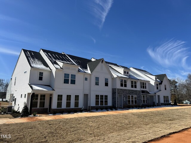 view of front of property featuring stone siding, brick siding, board and batten siding, and cooling unit