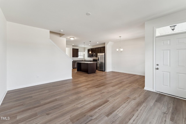 unfurnished living room featuring baseboards, recessed lighting, light wood-type flooring, and an inviting chandelier