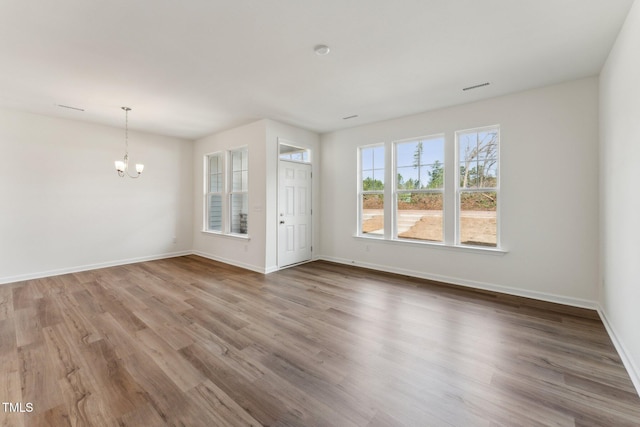 empty room with baseboards, visible vents, an inviting chandelier, and wood finished floors