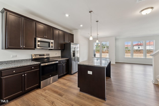 kitchen featuring dark brown cabinetry, appliances with stainless steel finishes, a center island, light stone countertops, and light wood-style floors