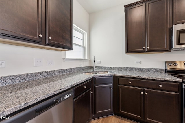 kitchen featuring stainless steel appliances, light wood-style floors, a sink, dark stone countertops, and dark brown cabinets