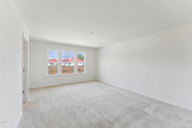 spare room featuring light carpet and baseboards