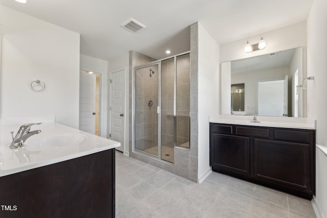 full bathroom featuring a stall shower, visible vents, two vanities, and a sink