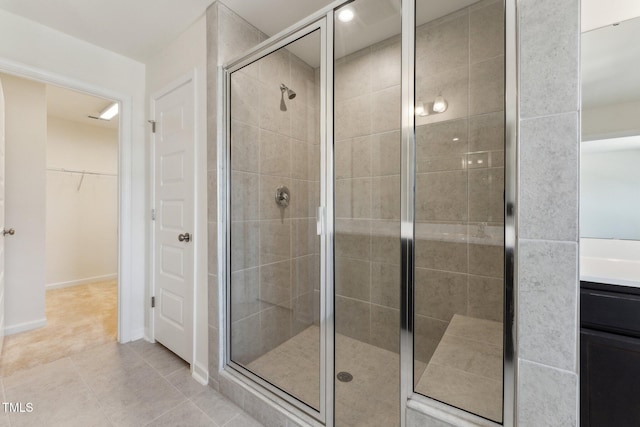 bathroom featuring vanity, baseboards, a spacious closet, tile patterned floors, and a stall shower