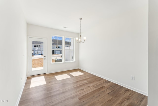 unfurnished dining area featuring a chandelier, wood finished floors, and baseboards