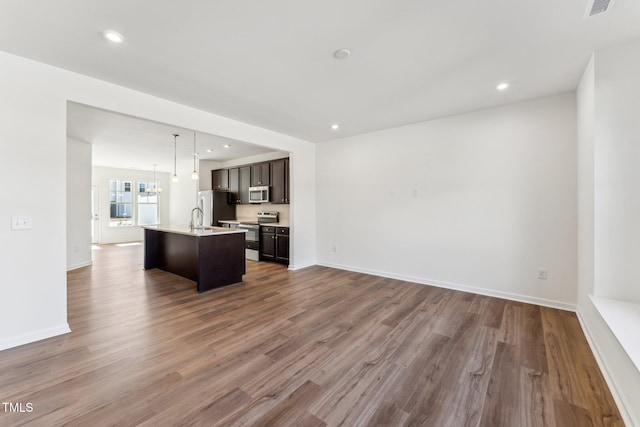 kitchen with a center island with sink, open floor plan, wood finished floors, light countertops, and stainless steel appliances