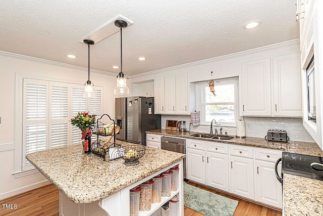 kitchen with appliances with stainless steel finishes, sink, white cabinets, a center island, and light hardwood / wood-style floors