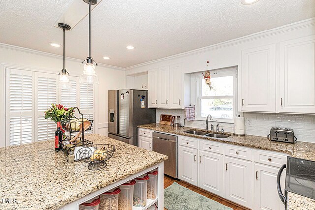 kitchen featuring white cabinetry, sink, hanging light fixtures, stainless steel appliances, and ornamental molding