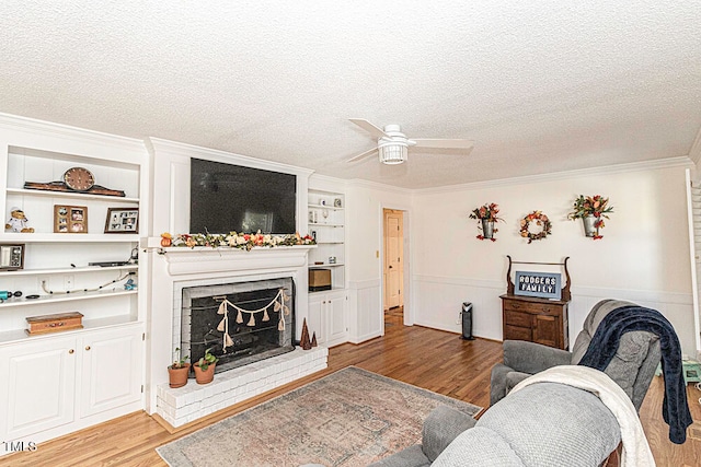 living room featuring a brick fireplace, ornamental molding, a textured ceiling, and light wood-type flooring