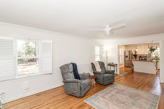 sitting room featuring a textured ceiling, light hardwood / wood-style flooring, ceiling fan, and crown molding