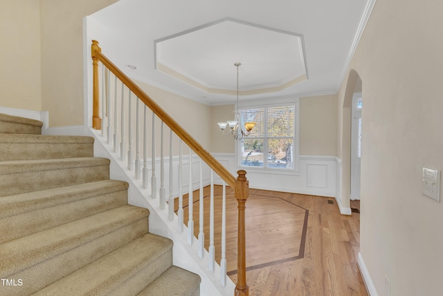 stairs featuring a raised ceiling, hardwood / wood-style floors, a chandelier, and ornamental molding