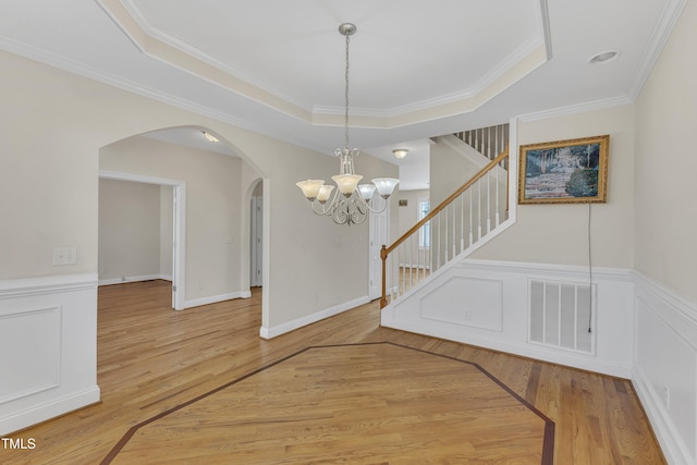 entrance foyer with ornamental molding, hardwood / wood-style flooring, a tray ceiling, and a notable chandelier