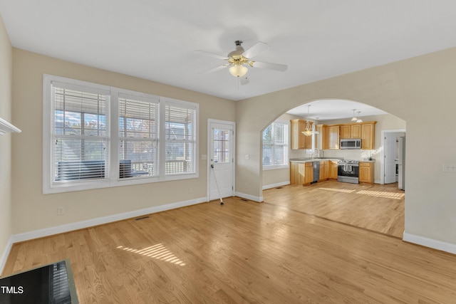 unfurnished living room with ceiling fan with notable chandelier, light wood-type flooring, and sink