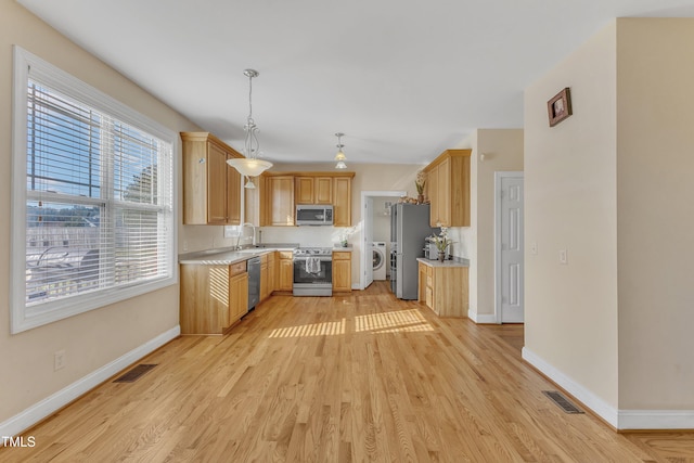 kitchen featuring washing machine and dryer, light wood-type flooring, sink, and appliances with stainless steel finishes