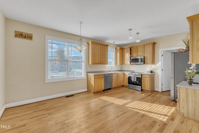 kitchen with light brown cabinetry, light hardwood / wood-style flooring, pendant lighting, and appliances with stainless steel finishes