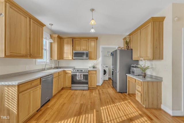 kitchen featuring pendant lighting, light hardwood / wood-style floors, washer / dryer, and stainless steel appliances