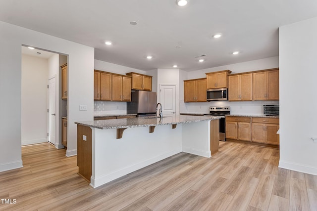 kitchen featuring light stone countertops, appliances with stainless steel finishes, light hardwood / wood-style floors, and a kitchen island with sink