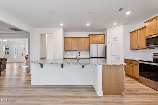 kitchen with light stone countertops, appliances with stainless steel finishes, light wood-type flooring, and an island with sink