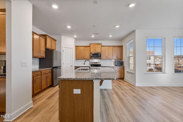 kitchen with light hardwood / wood-style floors, sink, stainless steel appliances, and an island with sink