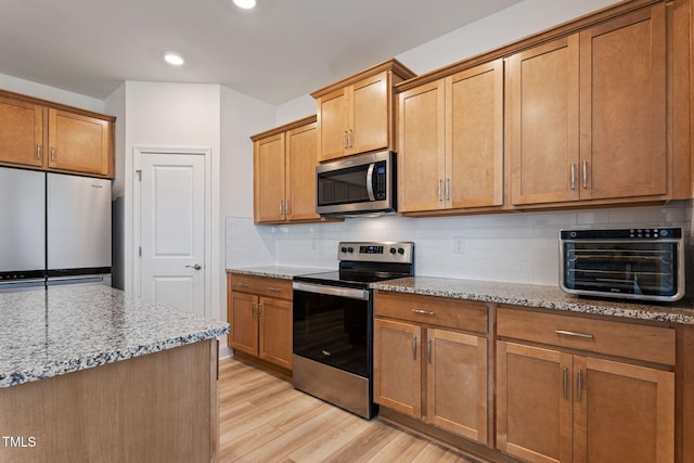 kitchen featuring appliances with stainless steel finishes, light hardwood / wood-style floors, light stone counters, and tasteful backsplash