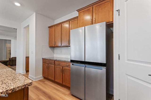 kitchen with light stone countertops, stainless steel fridge, light wood-type flooring, and decorative backsplash