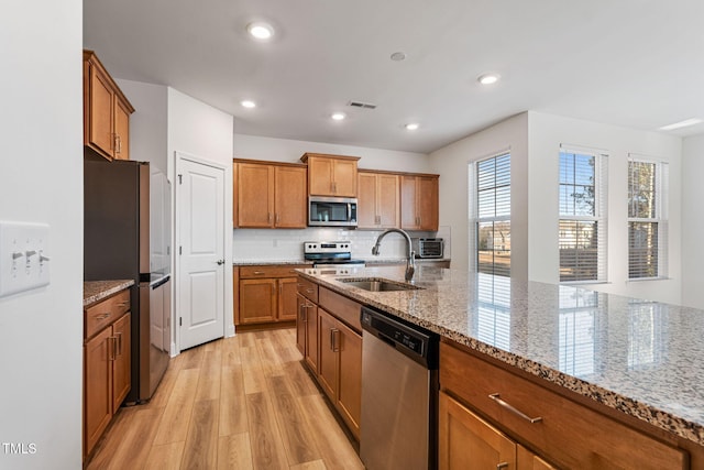 kitchen with backsplash, light stone counters, stainless steel appliances, sink, and light hardwood / wood-style flooring