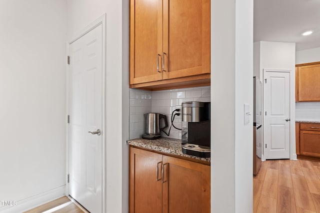 kitchen with tasteful backsplash, stainless steel refrigerator, light stone counters, and light wood-type flooring