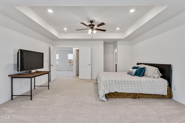 bedroom featuring a tray ceiling, light carpet, and ceiling fan