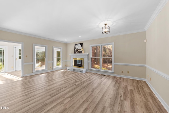 unfurnished living room with a brick fireplace, a notable chandelier, crown molding, and light hardwood / wood-style flooring