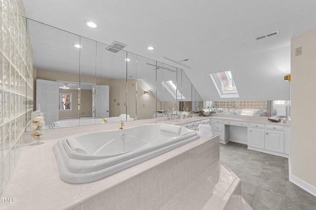 bathroom featuring vanity, tile patterned floors, vaulted ceiling with skylight, and tiled bath