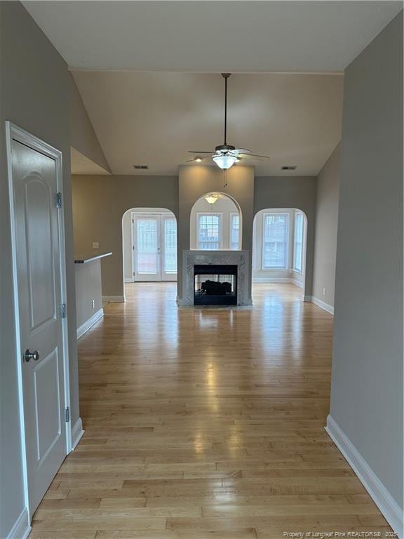 unfurnished living room with vaulted ceiling, ceiling fan, a high end fireplace, and light hardwood / wood-style floors