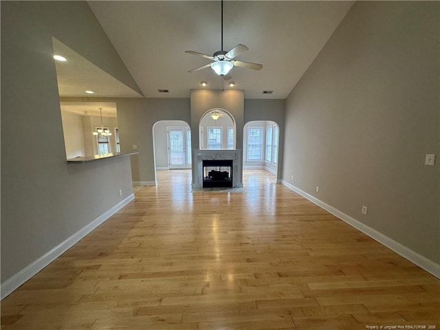 unfurnished living room with high vaulted ceiling, a high end fireplace, ceiling fan with notable chandelier, and light wood-type flooring