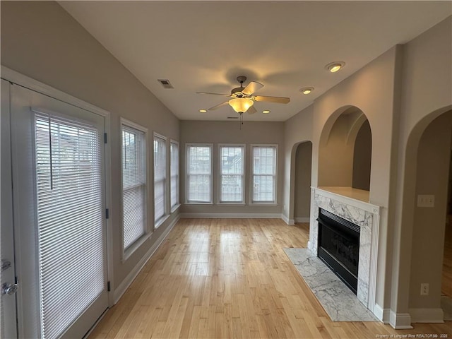 unfurnished living room featuring a healthy amount of sunlight, light wood-type flooring, ceiling fan, and a fireplace