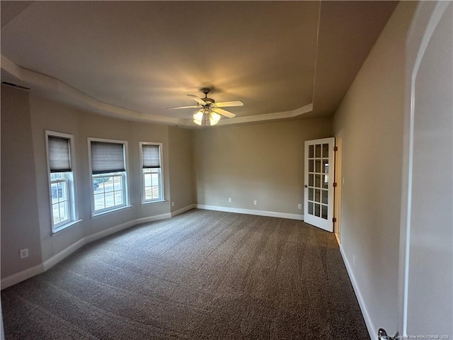 spare room with a raised ceiling, dark colored carpet, and ceiling fan