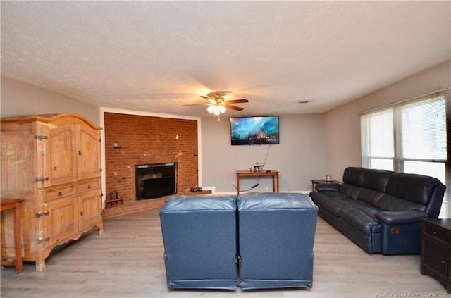 living room with ceiling fan, a fireplace, light hardwood / wood-style flooring, and a textured ceiling