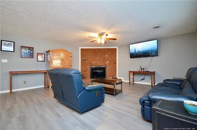 living room featuring wood-type flooring, ceiling fan, a fireplace, and a textured ceiling