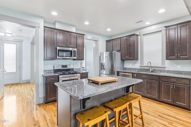 kitchen featuring a kitchen bar, sink, light hardwood / wood-style flooring, stainless steel appliances, and light stone counters