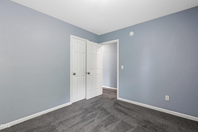 unfurnished bedroom featuring dark carpet, a textured ceiling, and a closet