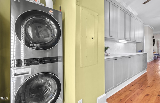 clothes washing area featuring stacked washer / drying machine, ornamental molding, electric panel, and light hardwood / wood-style flooring