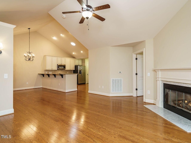 unfurnished living room with ceiling fan with notable chandelier, light hardwood / wood-style floors, a fireplace, and vaulted ceiling