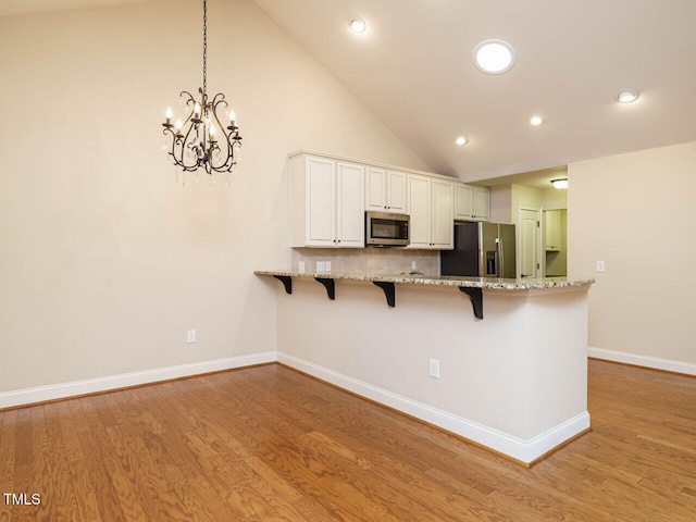 kitchen featuring a breakfast bar area, white cabinets, hanging light fixtures, and appliances with stainless steel finishes