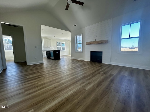 unfurnished living room featuring lofted ceiling, sink, dark hardwood / wood-style flooring, a fireplace, and ceiling fan with notable chandelier